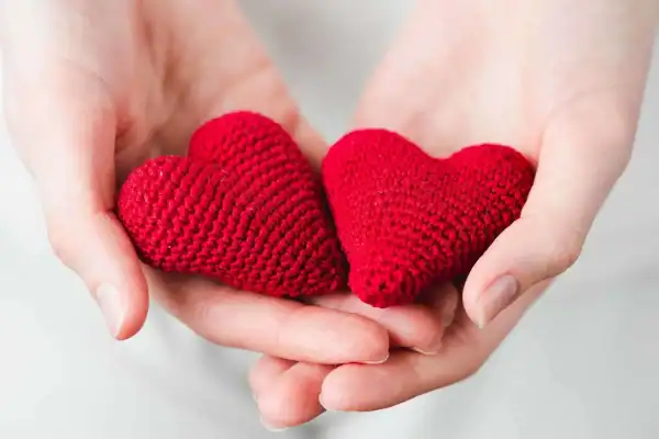 Cuori di stoffa rossi, simbolo di amore e affetto, tenuti delicatamente in mani gentili.