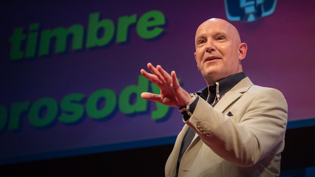 Bald man in beige suit speaking at a conference with "timbrate" and "prospy" in the background.