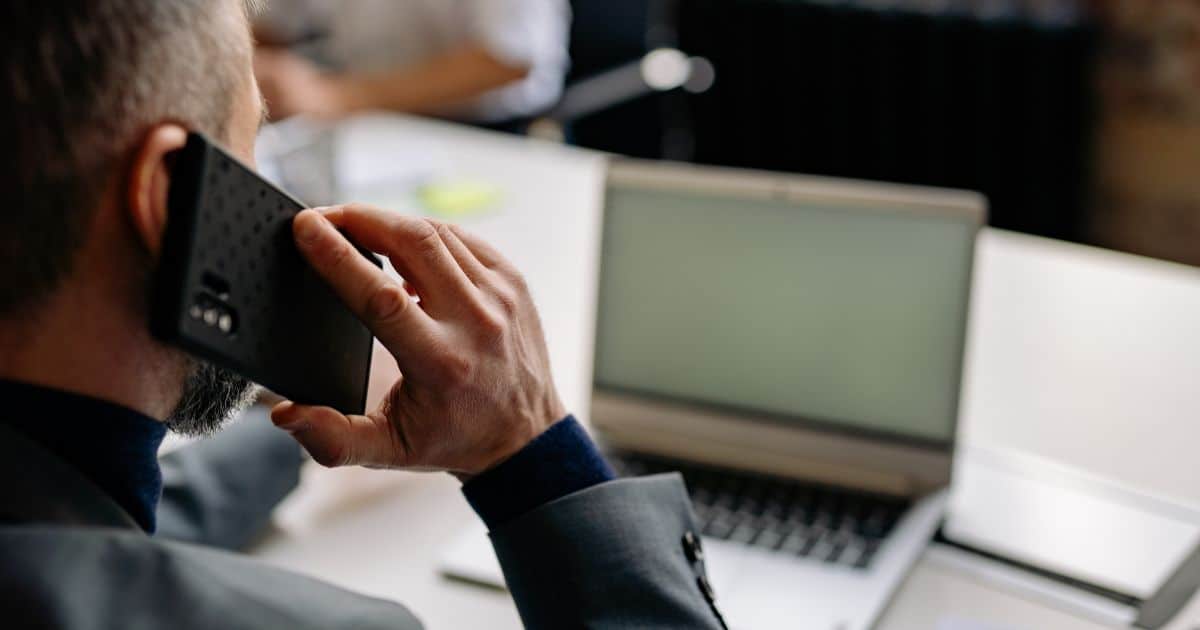Senior professional in a suit talking on the phone at a desk while exploring careers with an open laptop.