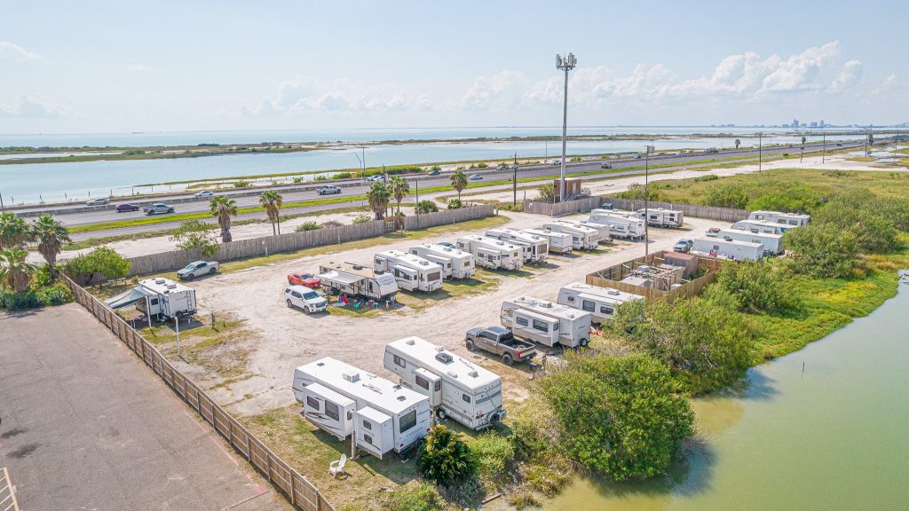 Portland, TX RV Park Aerial view of Portland RV Park in Portland, Texas, showing white trailers lined up near water, highway, and palm trees under clouds.