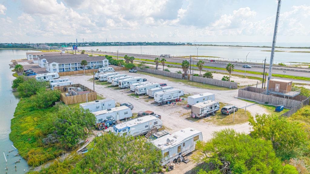 Portland, TX RV Park Aerial view of Portland RV Park in Portland, Texas, with rows of white RVs, palm trees, water nearby, and local buildings visible.