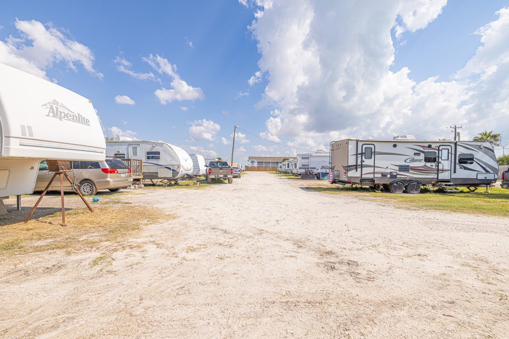 Portland, TX RV Park Portland RV Park in Portland, Texas on a sunny day with trailers, vehicles, gravel road, blue sky, and building in background.