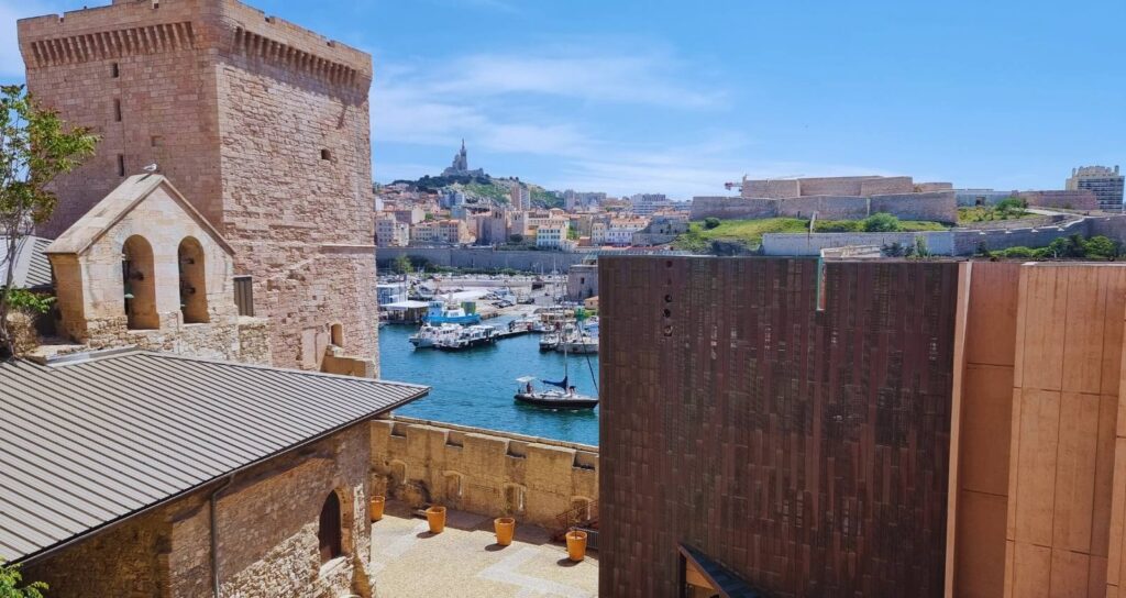 MuCEM Museum und Fort Saint-Jean in Marseille mit Hafenblick und Notre-Dame de la Garde auf dem Hügel im Hintergrund.