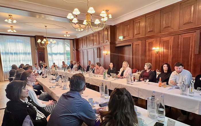 Chefetage des Deutschen Kitaverbandes bei einer Sitzung, Menschen diskutieren in elegantem Konferenzraum.