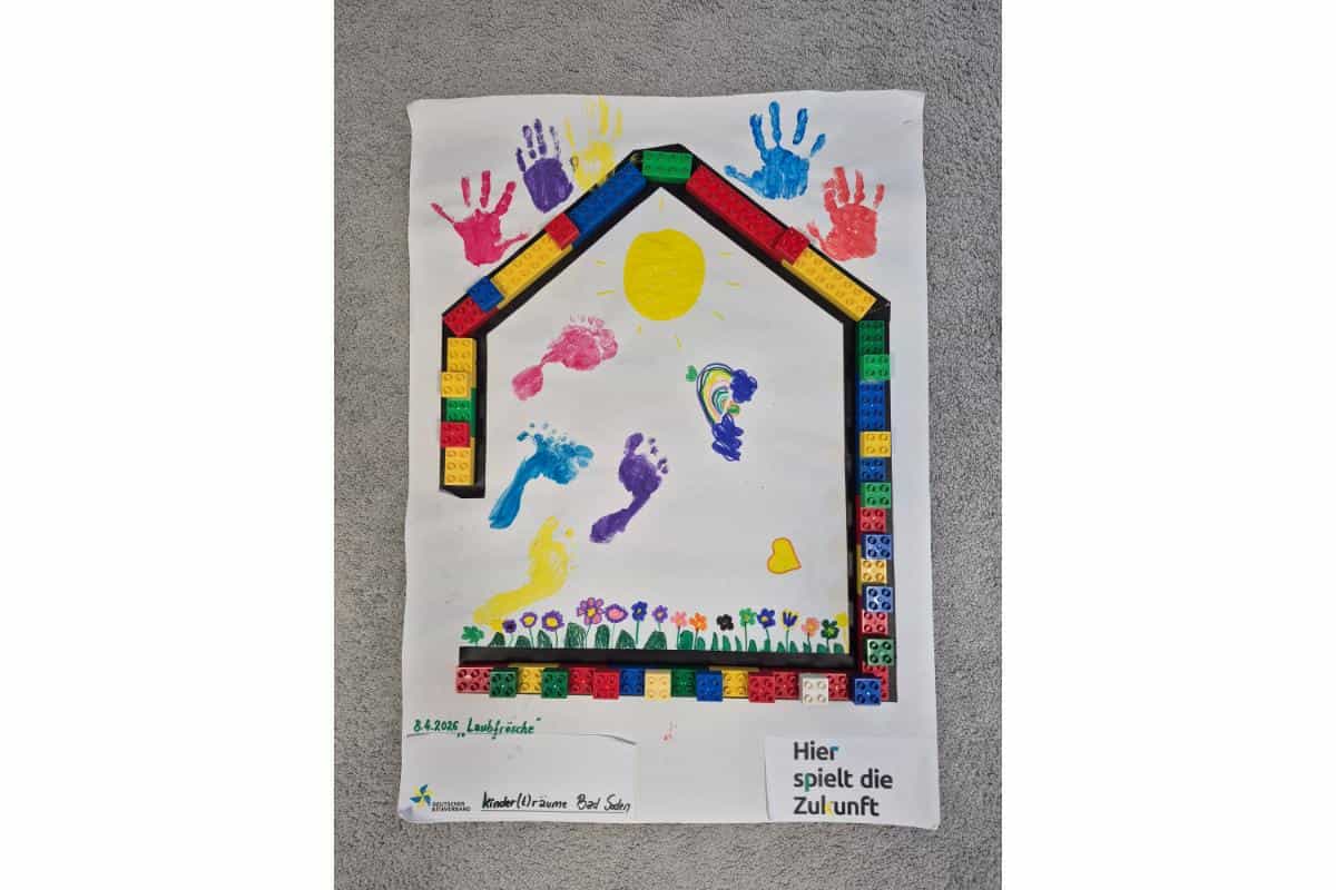 Haus aus Bauklötzen mit bunten Handabdrücken und Sonne, symbolisiert Gemeinschaft.