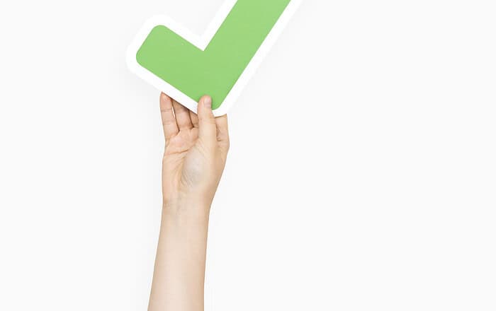 Hand hält grünen Haken, symbolisiert Unterstützung für verpflichtendes Kita-Jahr.