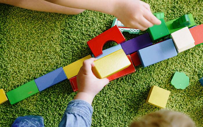Kinder spielen mit bunten Bauklötzen auf grünem Teppichboden.
