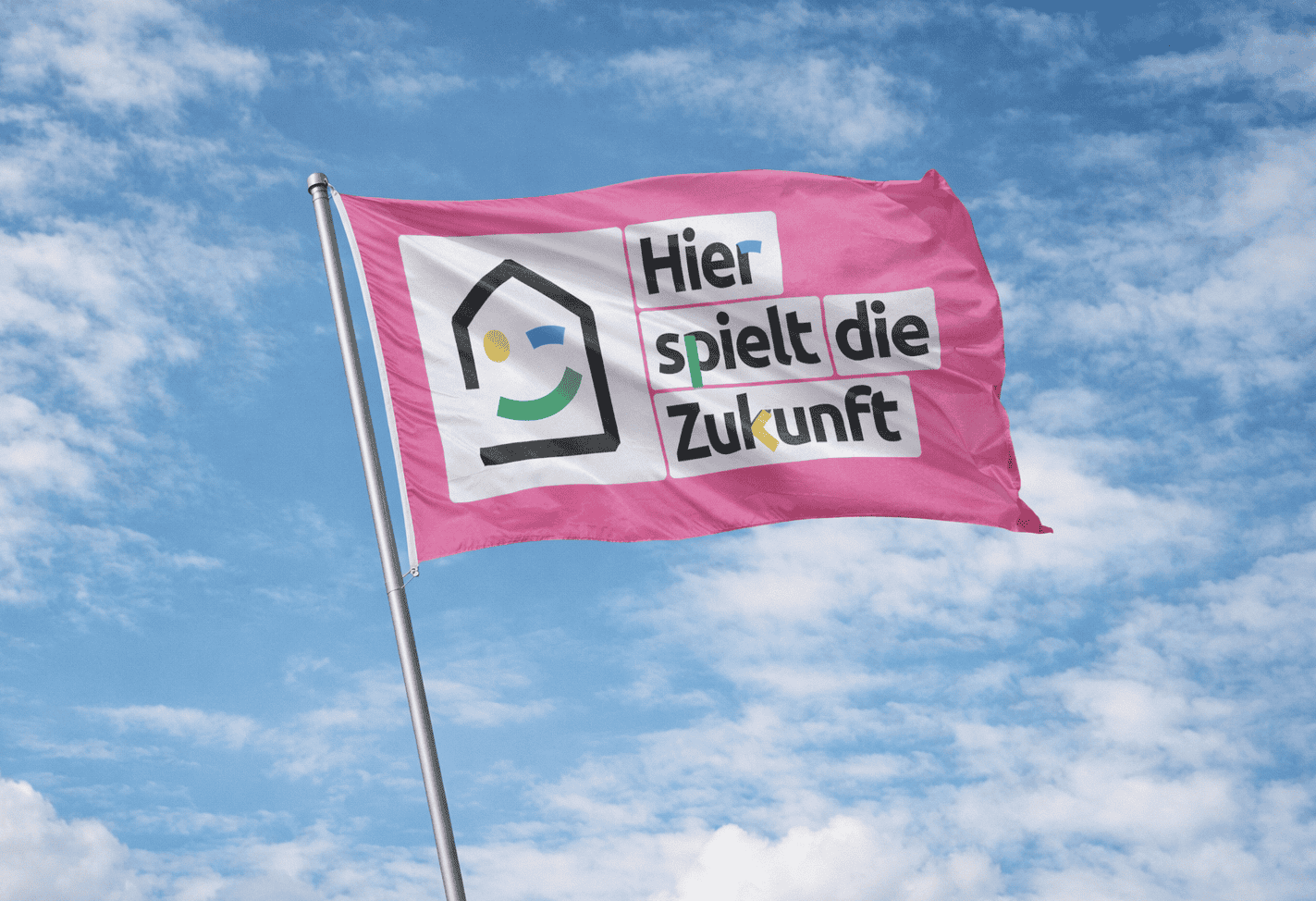 Ein farbenfrohes Banner mit dem Slogan "Hier spielt die Zukunft" weht im Wind vor einem blauen Himme.