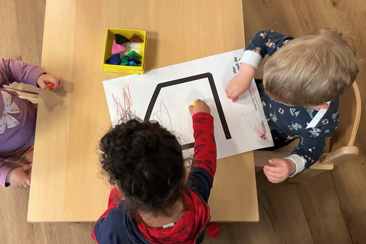 Kinder beim kreativen Malen mit bunten Stiften und Formen auf einem Tisch.