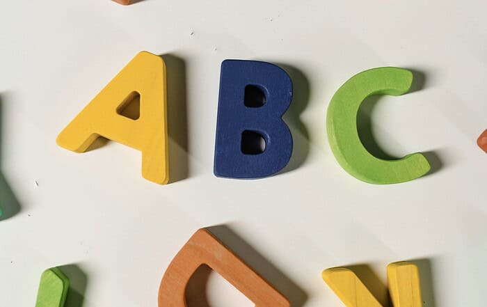 Lernbuchstaben aus Holz in bunten Farben auf weißem Hintergrund.