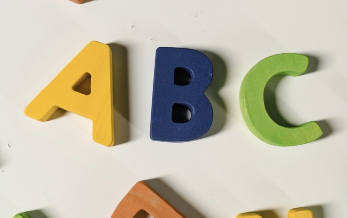 Lernbuchstaben aus Holz in bunten Farben auf weißem Hintergrund.
