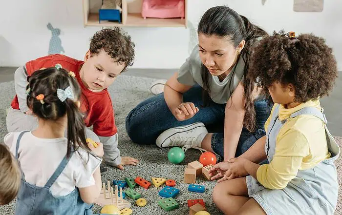 Kinder spielen mit bunten Bauklötzen und Bällen im Kindergarten, betreut von einer Erzieherin.