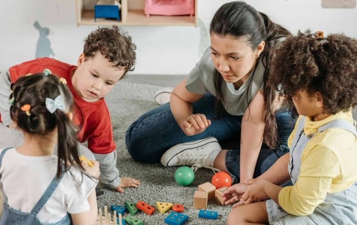 Kinder spielen mit bunten Bauklötzen und Bällen im Kindergarten, betreut von einer Erzieherin.