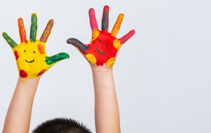 Kinderhände bemalt mit bunten Farben und lachenden Gesichtern.