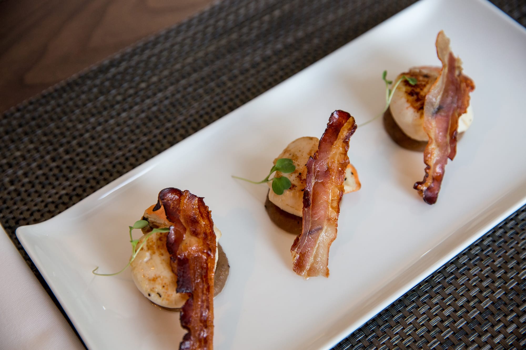 Elegant appetizer with bacon, potato, and microgreens on a white plate.
