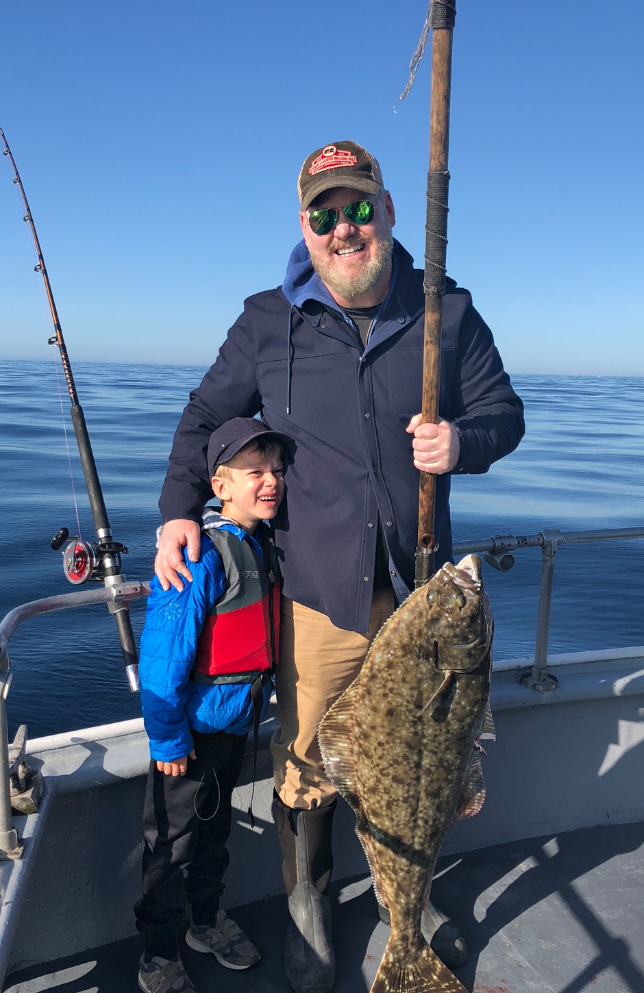 Jim and song standing on boat together holding giant fish