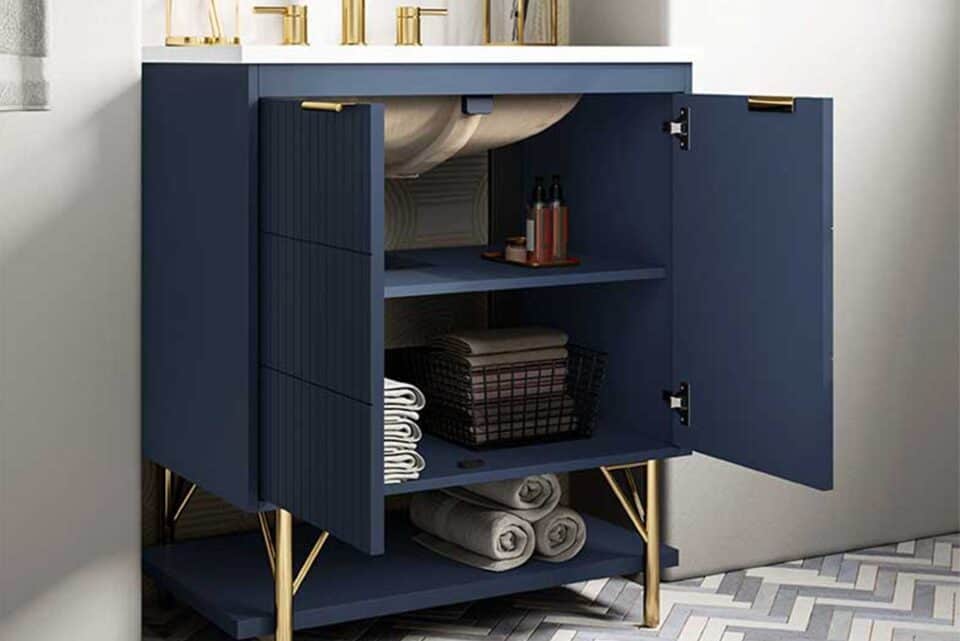 Open navy blue bathroom vanity cabinet with gold legs, displaying towels, toiletries, and a storage basket
