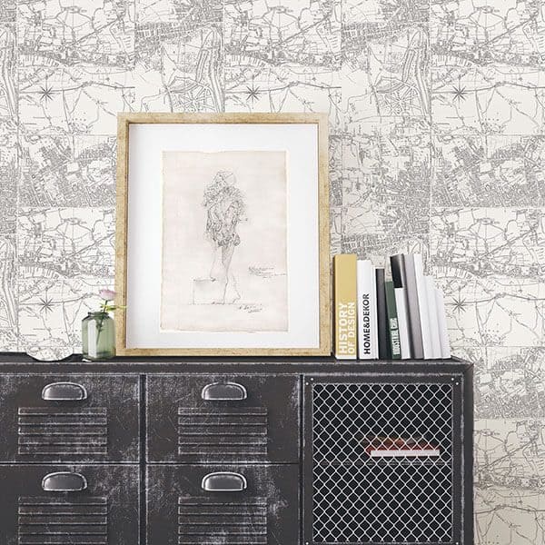 Black metal cabinet with a framed sketch, books, and a vase against a vintage map wallpaper