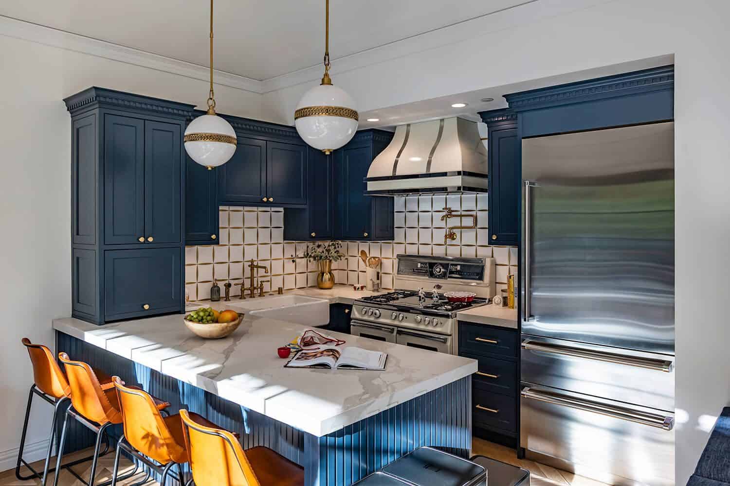 Kitchen with navy blue cabinets, white and gold accents, a marble countertop, and orange bar stools