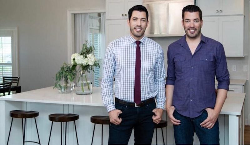 Drew and Jonathan standing in a modern white kitchen with bar stools and flowers