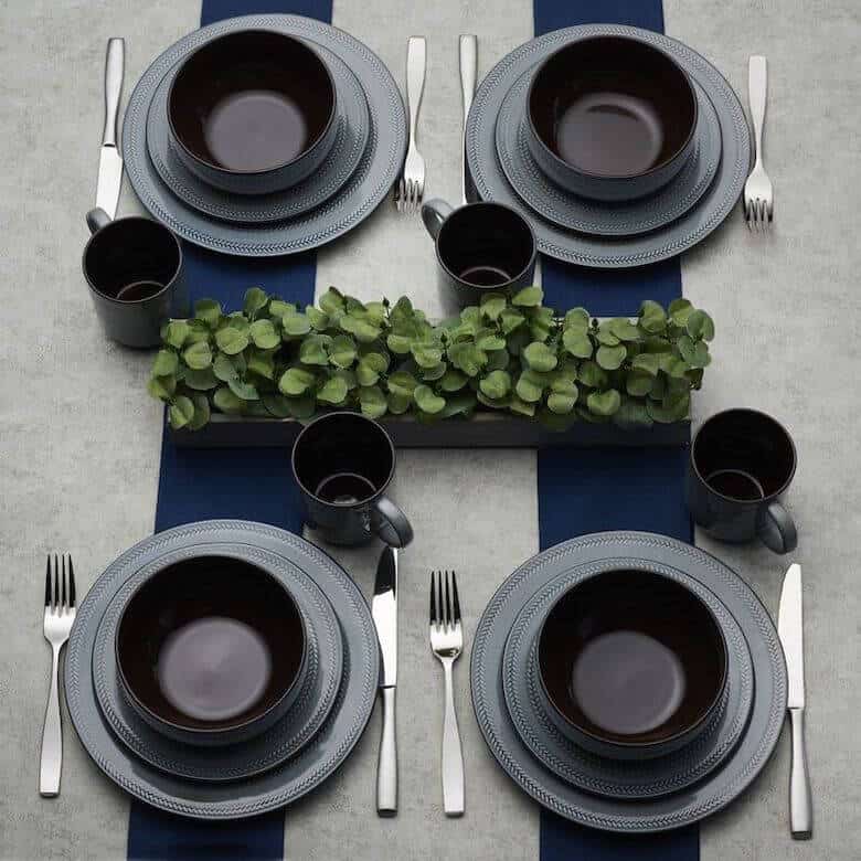 Modern table setting for four with dark dinnerware, silver flatware, and a green centerpiece on a navy-striped tablecloth