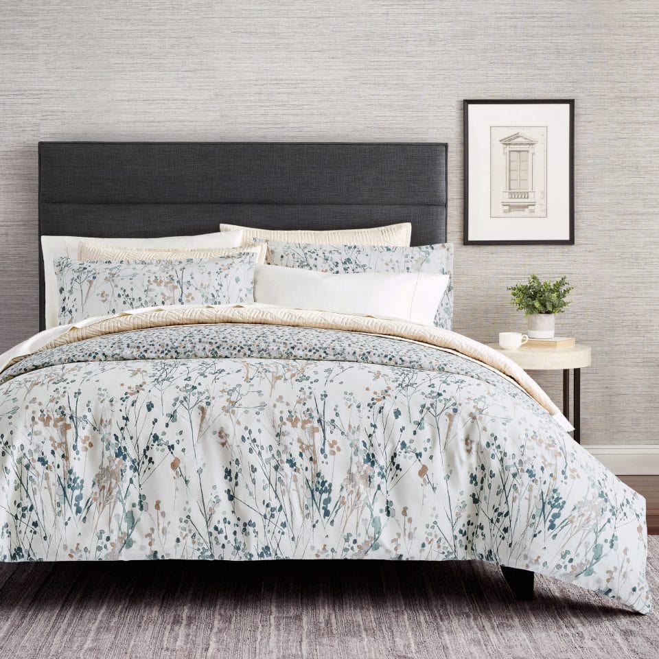 Floral patterned bedding with matching pillows and side table with plant and artwork