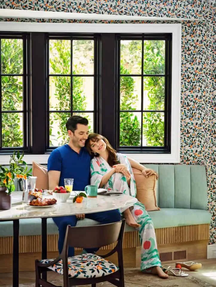 Jonathan and Zooey sitting in a cozy breakfast nook with floral wallpaper, and black windows