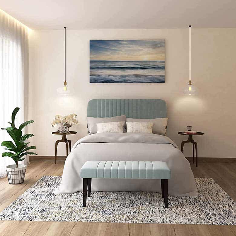 Bedroom with a light blue upholstered bed, matching bench, pendant lights, and ocean artwork above the bed