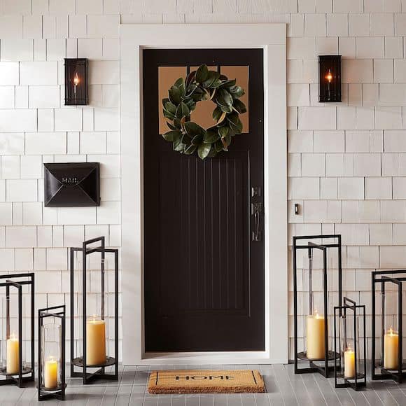 Black door with wreath, candles, and doormat