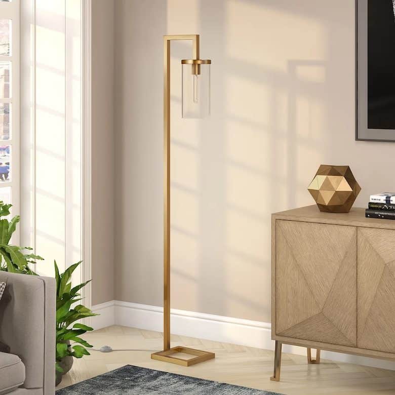 Modern living room corner with gold floor lamp, geometric decor, and wooden cabinet