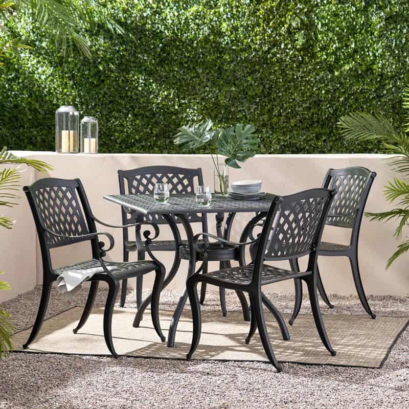 Outdoor patio set with black metal lattice table and four matching chairs on a woven rug