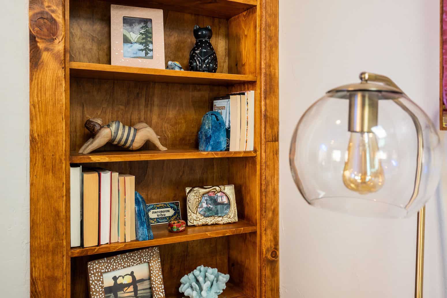 Wooden bookshelf with various decor, including books, framed photos, sculptures, and blue crystals