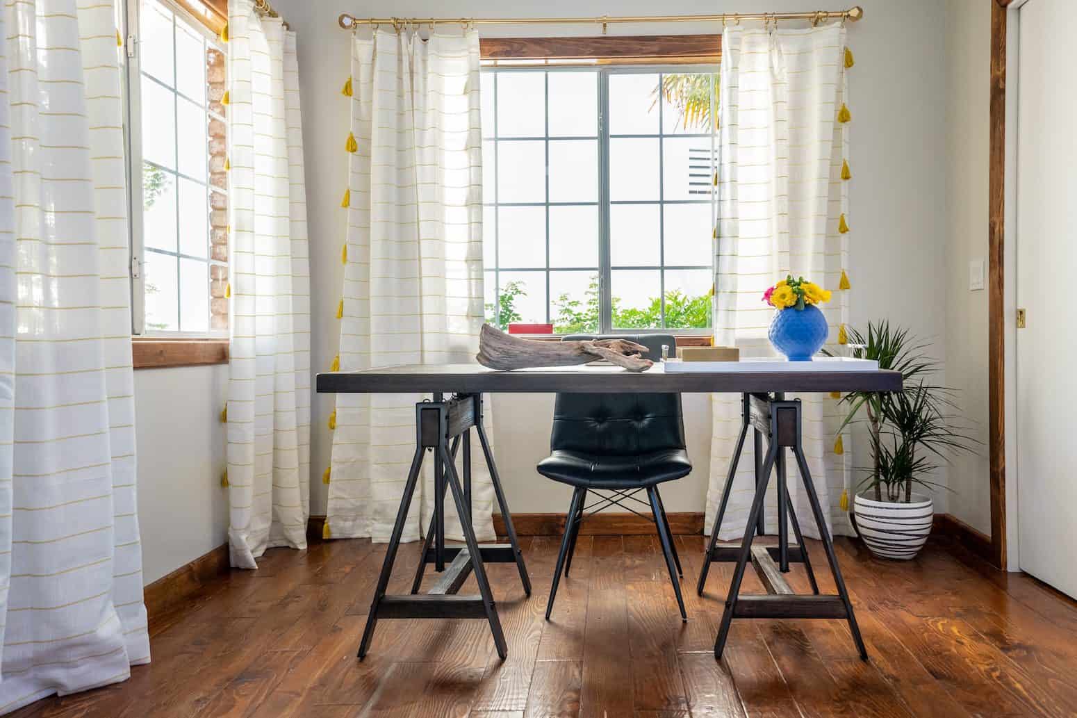 Minimalist workspace featuring a black chair, a desk with unique sawhorse legs, and a large window
