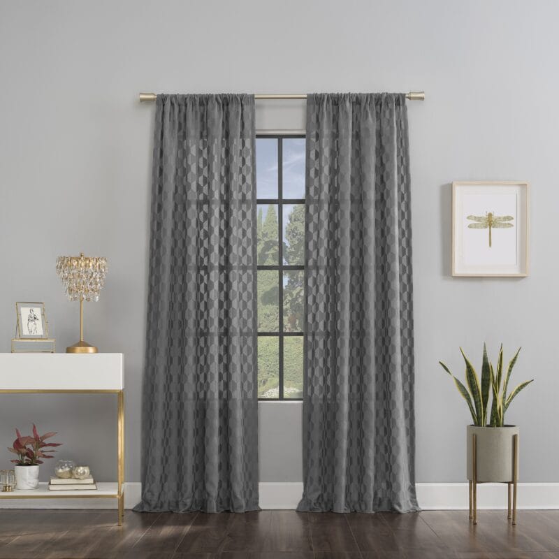 Sheer gray curtains with geometric pattern hanging on a brass rod in a modern living space