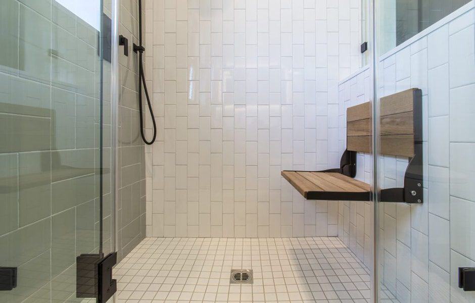 Walk-in shower with white tiles, fold-down bench, and black fixtures.