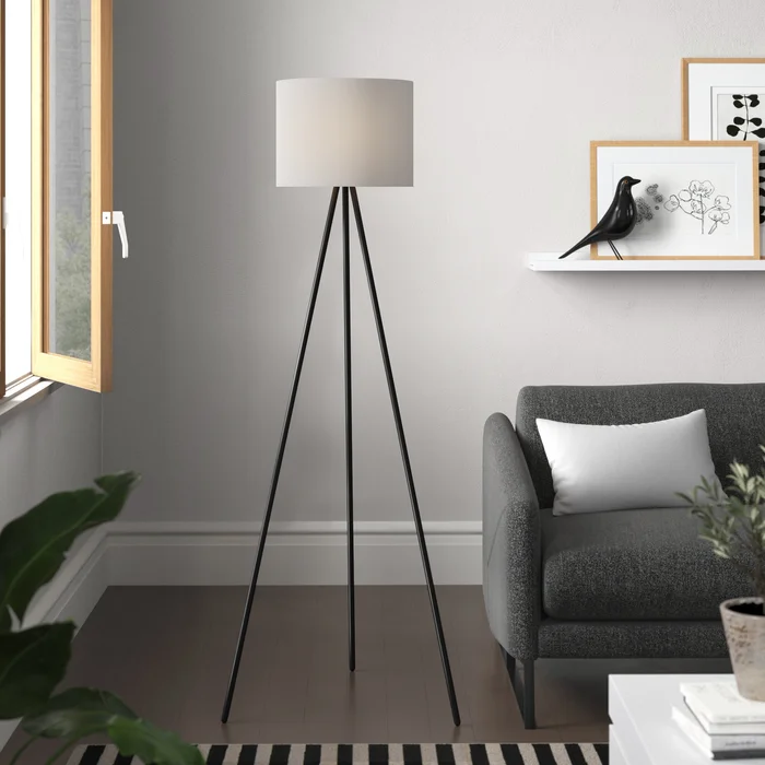 Tripod floor lamp beside a dark grey armchair and wall shelf with framed artwork