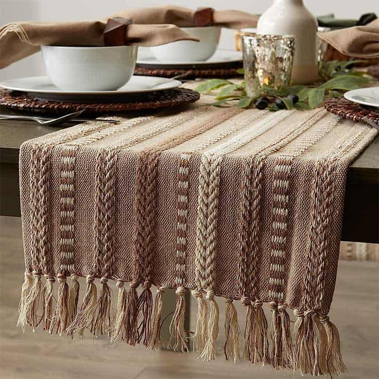 Woven table runner with neutral-toned stripes and fringe on a set dining table