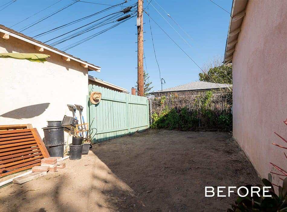 Empty backyard space with dirt ground, a green fence, and utility equipment