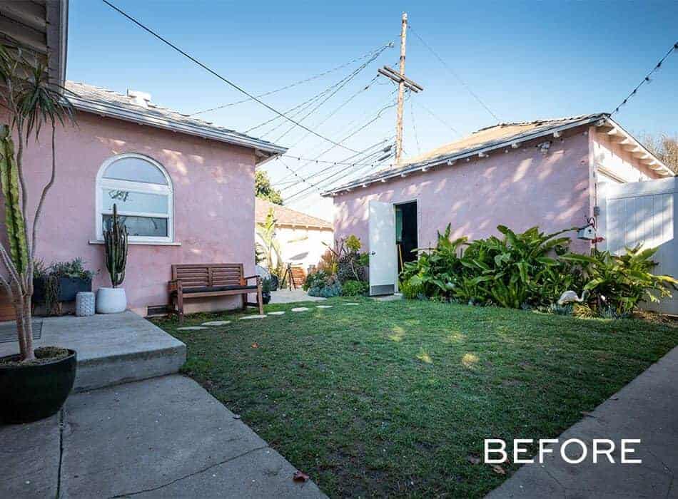 Backyard with a patchy lawn, pink stucco buildings, potted plants, and a wooden bench.