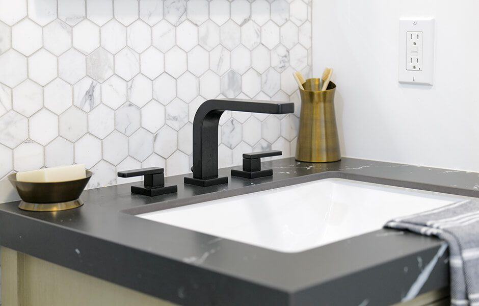 Bathroom sink with black fixtures, marble hexagonal backsplash, and gold accents