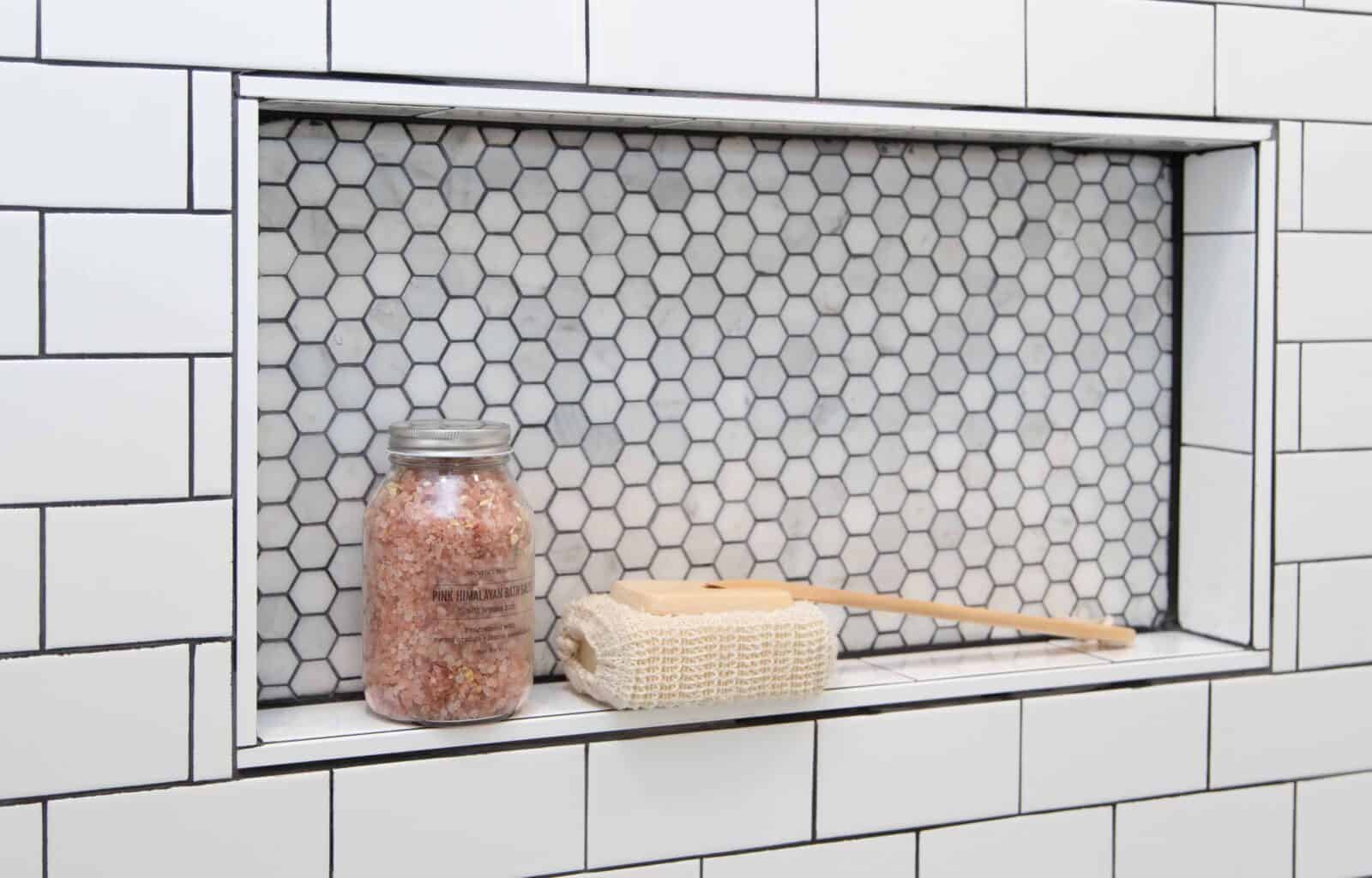 Shower niche with hexagon tile, holding pink Himalayan bath salts and a bath scrub brush