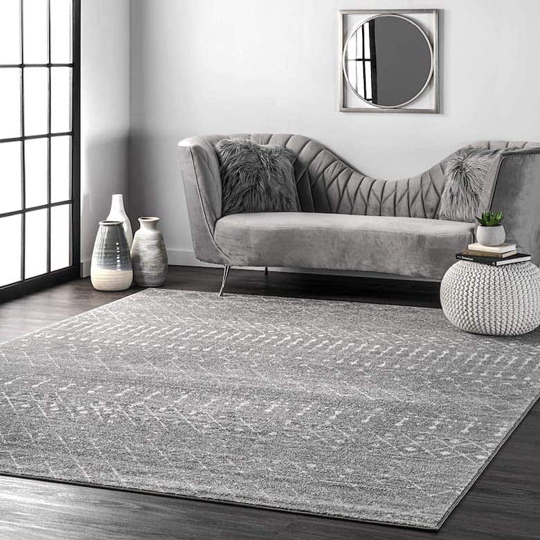 Gray velvet couch, mirror, knitted pouf, vases, and patterned rug