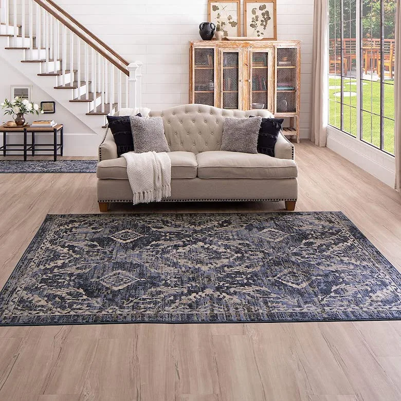 Living room with a blue rug, patterned couch, and wooden stairs leading to the second floor.