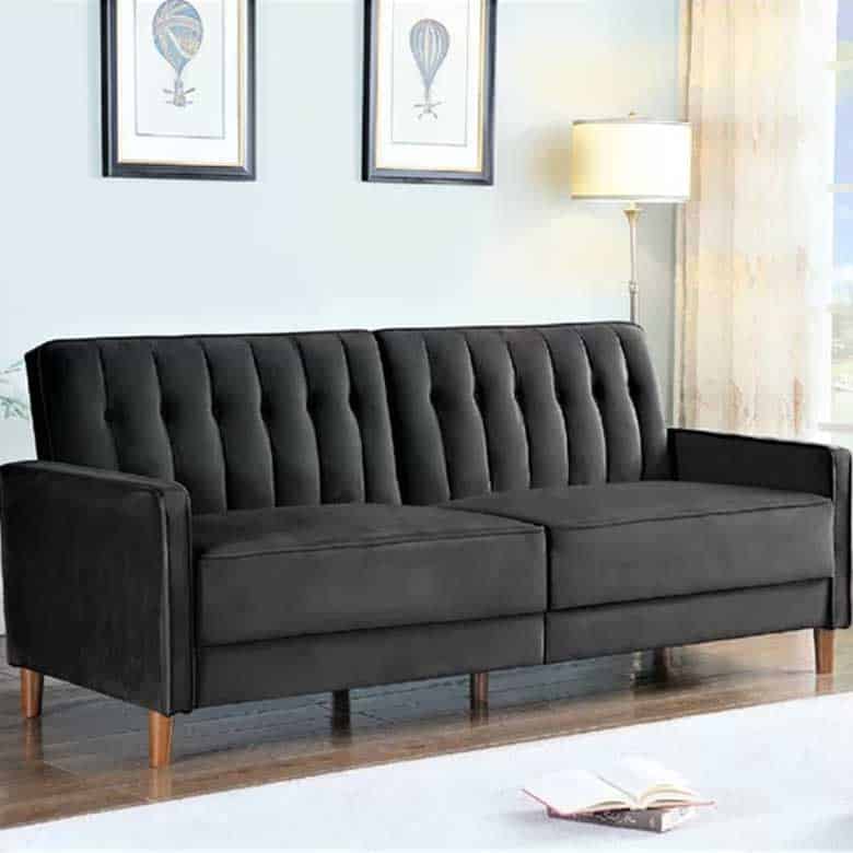 Black tufted sofa with wooden legs, in a light room with artwork and a lamp