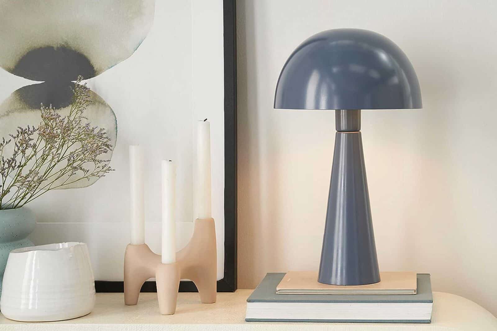 A lamp, candles, a vase, and books, spaced out atop a modern desk