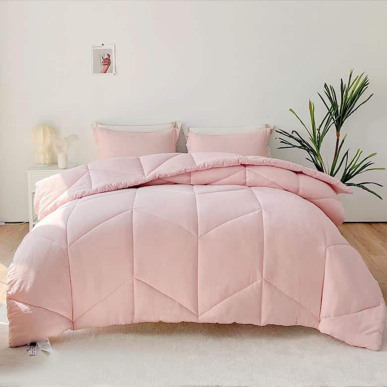 Neatly made bed with pink comforter in a white room