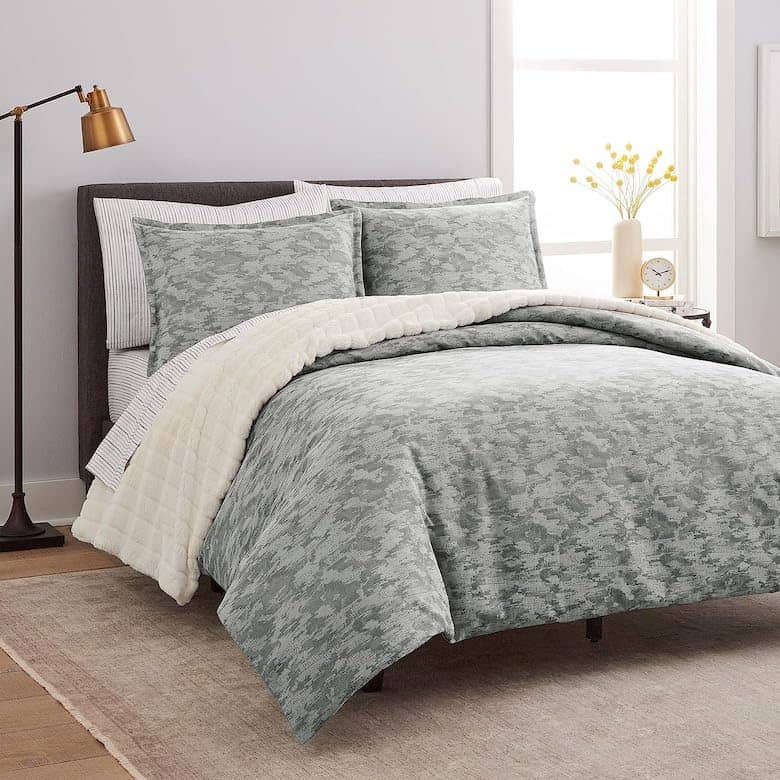 Modern bedroom with gray patterned bedding, white throw blanket, and floor lamp