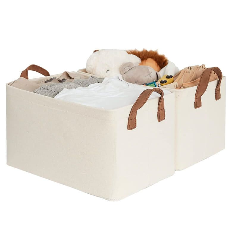 Two fabric storage bins filled with clothes and stuffed animals, with leather handles
