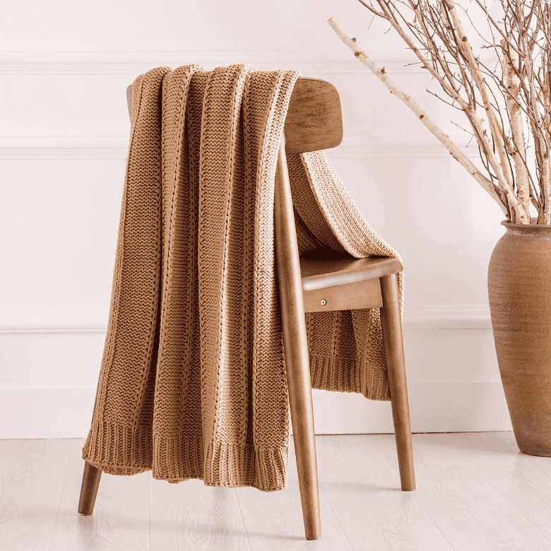 Knit throw on wooden chair beside vase with branches