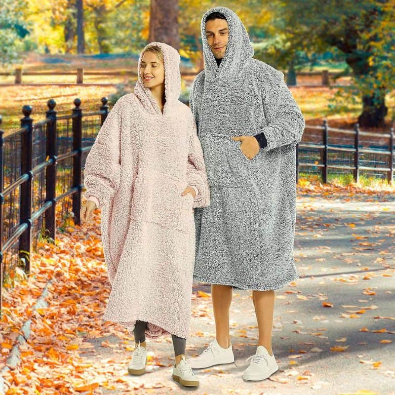 Couple wearing oversized hooded blankets while walking on a leaf-covered path in autumn